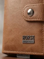 لقطة مقربة تبرز صفيحة الشعار المعدني لـ Horse Imperia وزر القفل الكبسولة على محفظة وحامل كروت فوليو من براند Quorvella.